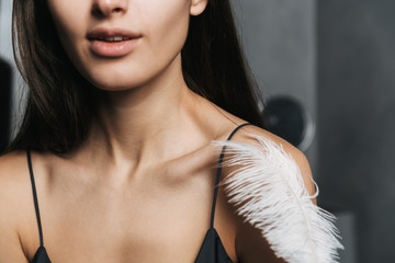 Photo of caucasian woman with long dark hair and clean skin touching her body with big feather,...