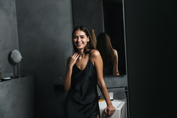 Smiling young woman standing at the mirror at the bathroom
