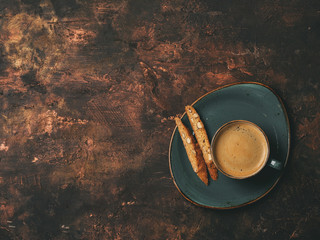 Biscotti cookies with almonds and one cup of coffee espresso on dark copper background with copy space. Flat lay.