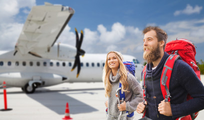 travel, tourism and people concept - couple of tourists with backpacks over plane on airfield background