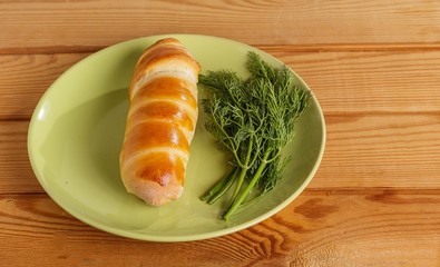 Sausage baked in dough and dill on a plate on the table.