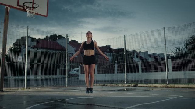 Beautiful Energetic Fitness Girl Skipping/Jumping Rope. She is Doing a Workout in a Fenced Outdoor Basketball Court. Evening Footage After Rain in a Residential Neighborhood Area.