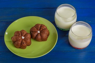 Two cakes on a plate and two glasses of milk on the table.