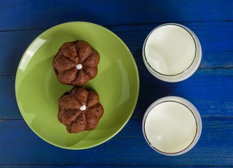 Two cakes on a plate and two glasses of milk on the table.