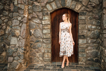 Fototapeta na wymiar beautiful girl in a dress outdoors, amazing woman on the background of the old door of a stone wall