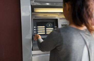 finance, cryptocurrency and technology concept - close up of woman at atm machine with bitcoin icon on screen