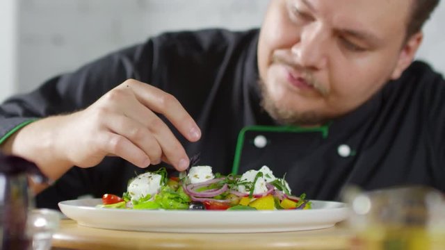 Close up shot of bearded male restaurant chef putting basil leaf on Greek salad before serving it
