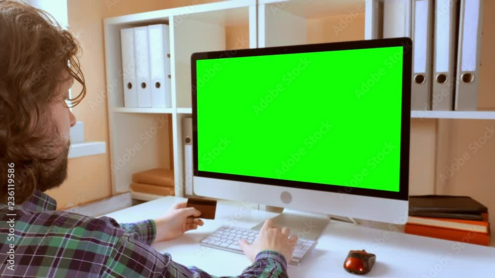 Aufkleber man sitting at workplace paying game on computer in small office. businessman with beard looking on display with green screen. employee in startup company typing on keyboard use pc mouse