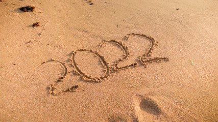 Closeup photo of 2022 numbers written on wet sand on the ocean beach. Concept of New Year, Christmas and travel on winter holidays.