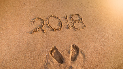 Closeup image of 2018 numbers and footprints on wet sand on the island beach. Concept of New Year, Christmas and travel on winter holidays.
