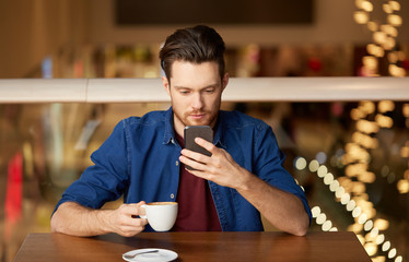 people, technology and leisure concept - man drinking coffee and messaging on smartphone at restaurant or cafe