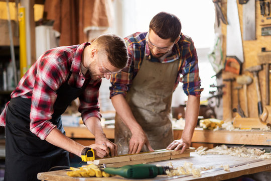 profession, carpentry, woodwork and people concept - two carpenters with ruler measuring wooden board at workshop