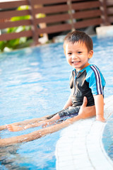A toddler boy sitting on the edge of a swimming pool