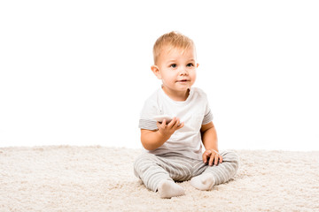 adorable toddler boy with smartphone sitting on carpet isolated on white