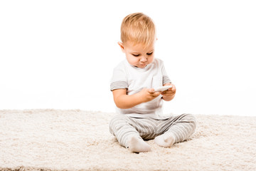 adorable little boy with smartphone sitting on carpet isolated on white