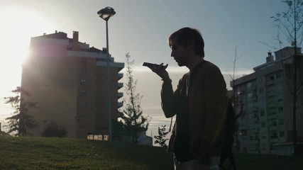 Handsome stylish man student freelancer leaving message using voice recognition, speaking at smartphone on street. Helper find city background - Powered by Adobe