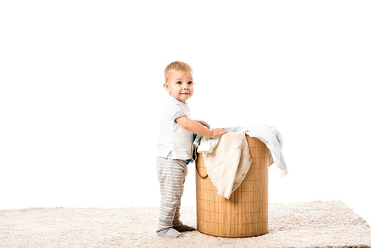 Toddler Boy Standing In Front Of Wicker Laundry Basket And Smiling Isolated On White