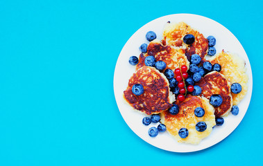 Cottage cheese pancakes with blueberry and red currant on blue background, breakfast or lunch