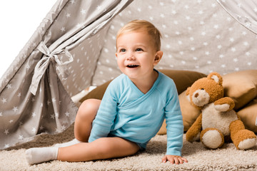 toddler boy sitting in baby wigwam with pillow and teddy bear and laughing isolated on white © LIGHTFIELD STUDIOS