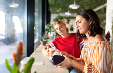 people, cash payment and finances concept - female friends paying in dollar money for coffee at cafe