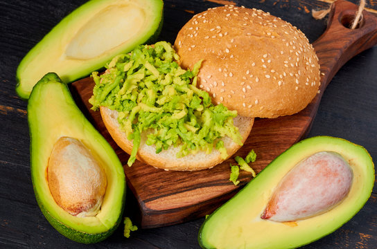 Healthy avocado burger on the wooden board - traditional Mexican dish. Vegetarian green sandwich on the black kitchen background. Close up view