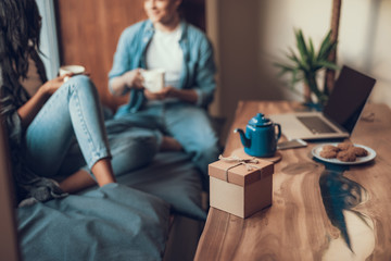 Obraz premium Two young couple enjoying their romantic date and drinking tea on the window sill while having beautiful gift box on the table