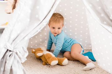 cute toddler boy in blue bodysuit sitting on carpet in baby wigwam © LIGHTFIELD STUDIOS