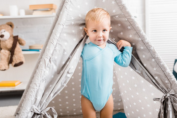 cute toddler boy in blue bodysuit standing in baby wigwam © LIGHTFIELD STUDIOS