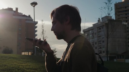 Handsome stylish man student freelancer leaving message using voice recognition, speaking at smartphone on street. Helper find city background - Powered by Adobe