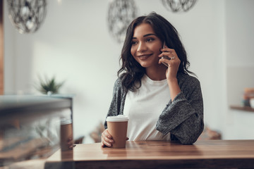 Peaceful relaxed young lady smiling and holding her carton cup of coffee while having a pleasant...