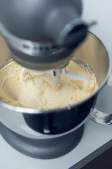 An industrial kitchen food mixing machine whipping and mixing sweet creamy fluffy light cake mixture, in a silver metal bowl.