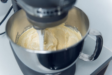 An industrial kitchen food mixing machine whipping and mixing sweet creamy fluffy light cake mixture, in a silver metal bowl.
