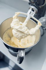 An industrial kitchen food mixing machine whipping and mixing sweet creamy fluffy light cake mixture, in a silver metal bowl.