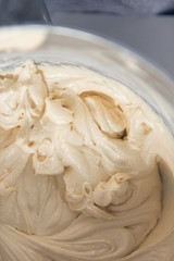 A close up of An industrial kitchen food mixing machine whipping and mixing sweet creamy fluffy light cake mixture, in a silver metal bowl.