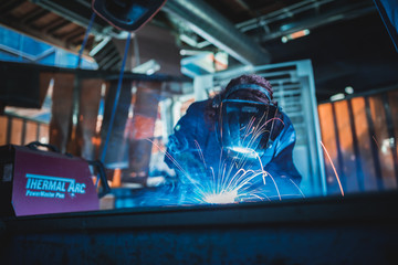 london, england, 02/02/2018 A vibrant action shot of a skilled working metal welder in action, welding metal. Photographed with a slow shutter speed and spark trails. Orange and teal. - obrazy, fototapety, plakaty