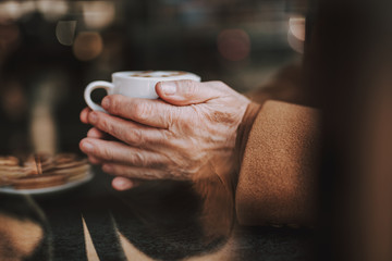 Fototapeta na wymiar : Enjoying favorite beverage. Close up of senior man hands with white cup of cappuccino