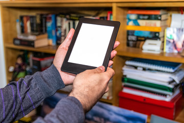 Male hands holding digital reading device in front of bookshelves
