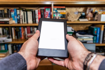 Male hands holding digital reading device in front of bookshelves
