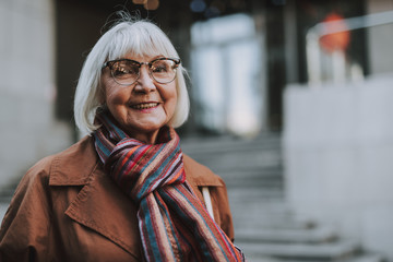 Portrait of stylish old lady in coat looking at camera and smiling. Copy space in right side