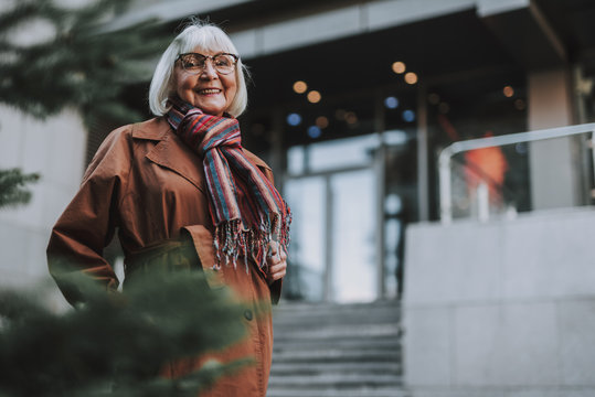 Waist Up Portrait Of Charming Old Lady In Coat Looking At Camera And Smiling. Copy Space In Right Side