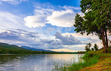 Landscape scene of lake, tree and  mountain in cloudy sunset sky.