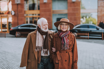 Portrait of handsome bearded man holding hand of his wife while looking at her and smiling. Lady wearing hat and glasses