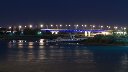 Fototapeta na wymiar Ship and illuminated bridge on the riverside Ural in city Atyrau timelapse hyperlapse