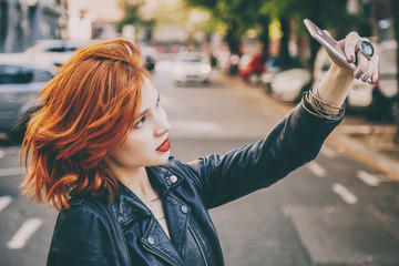 portrait of fashionable young woman wearing a leather jacket taking selfie with smartphone