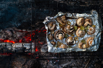 Baked mushrooms in foil on grill on coals. Lunch tourist in forest