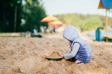 Child playing with sand near lake on cool day