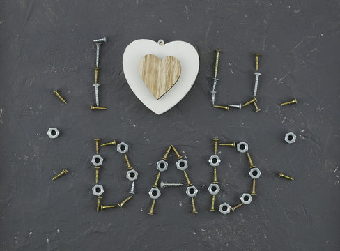 Text "i love you Dad" for father's day with heart and lettering composition made from screws, screws, nut, nails, screws, washers on dark background. Top view flat lay
