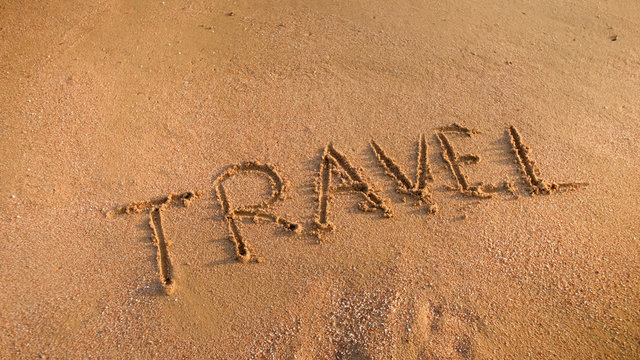 Closeup photo of word Travel written on wet beach sand. Concept of tourism, traveling, trips and journeys.