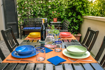 Table set for four diners. Dishes, cutlery and drinks waiting for guests. Waiting for friends for an outdoor lunch. Convivial moments to share with dear friends at home.