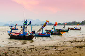 Small fishing boats anchor at beach in cloudy sunset sky.